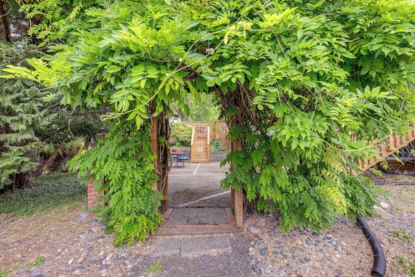 A wooden archway leading to a covered patio area with a brick wall and a wooden fence in the background. - Unique Unit w/ Patio & Grill in Portland Area! (Milwaukie)