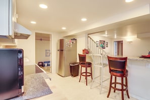 A kitchen with a refrigerator, two bar stools, a trash can, and a staircase leading to another level. - Unique Unit w/ Patio & Grill in Portland Area! (Milwaukie)