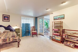 A bedroom with a bed, a chair, a bookshelf, and a door leading to a balcony. - Unique Unit w/ Patio & Grill in Portland Area! (Milwaukie)