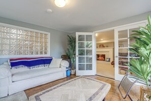 A living room with a sofa, a coffee table, a potted plant, and a door leading to another room. - Unique Unit w/ Patio & Grill in Portland Area! (Milwaukie)