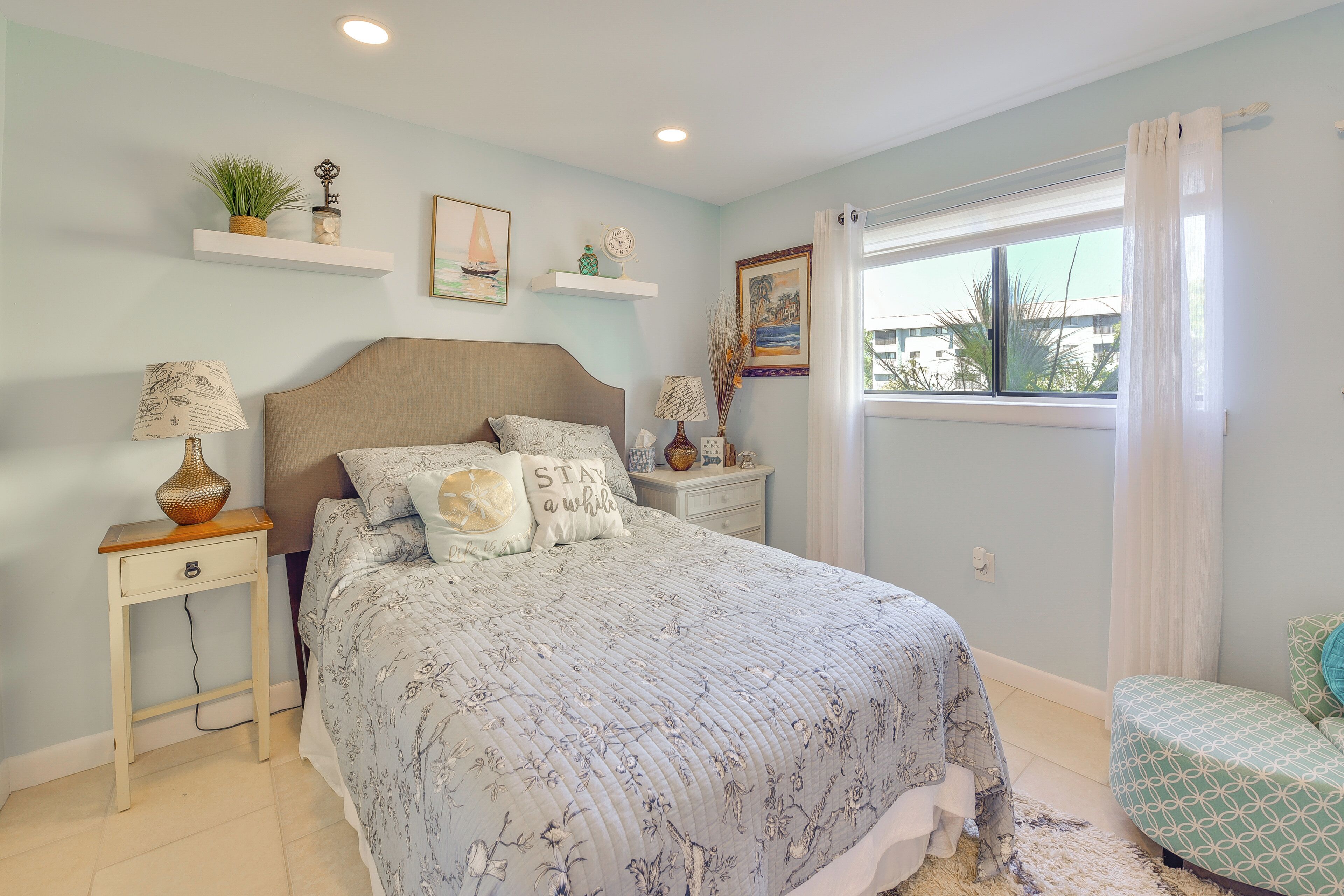 A bedroom with a bed, bedside tables, a window with curtains, a small chair, and a view of the outside.