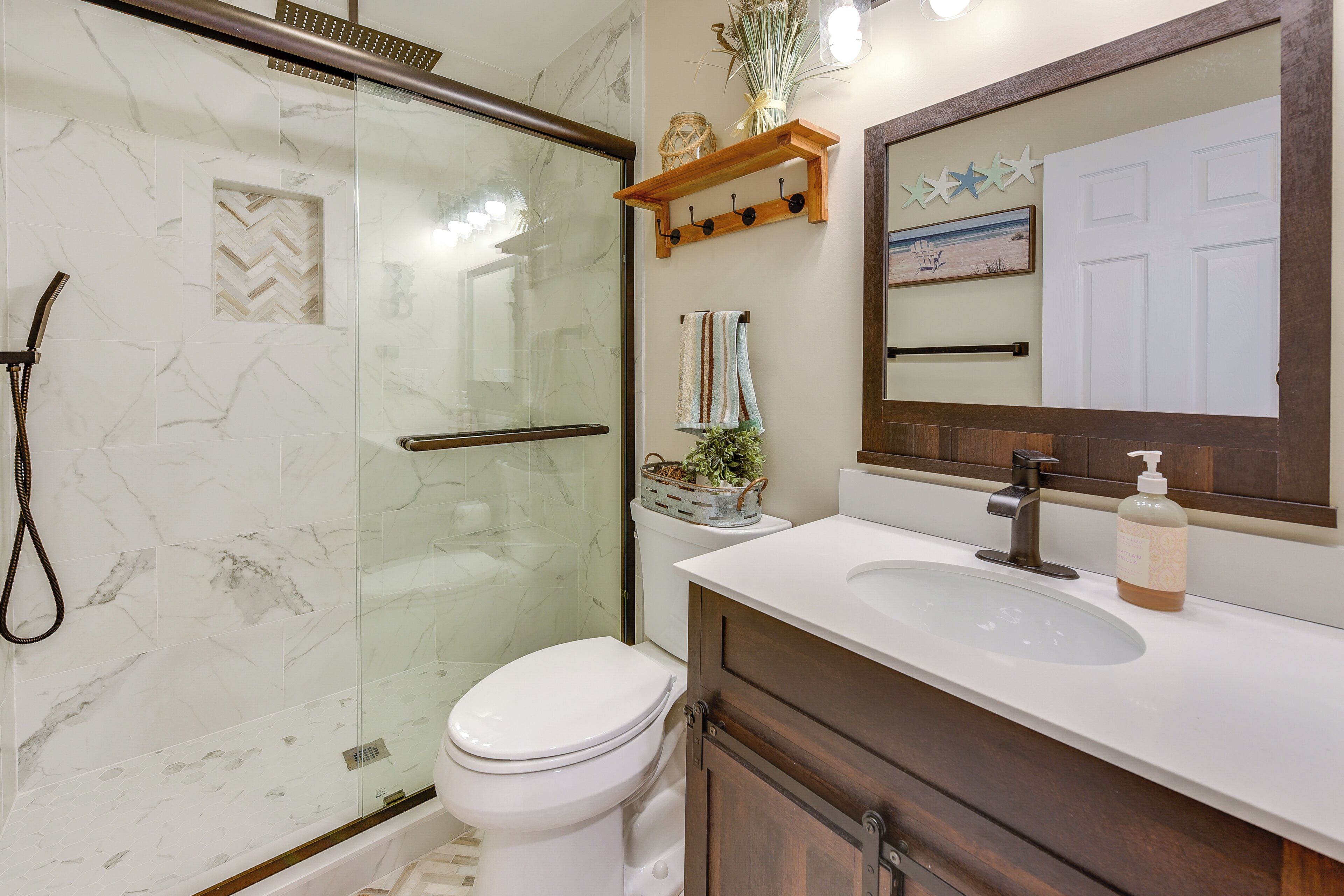 A bathroom with a glass shower enclosure, a white toilet, a wooden vanity with a mirror, and a towel rack.