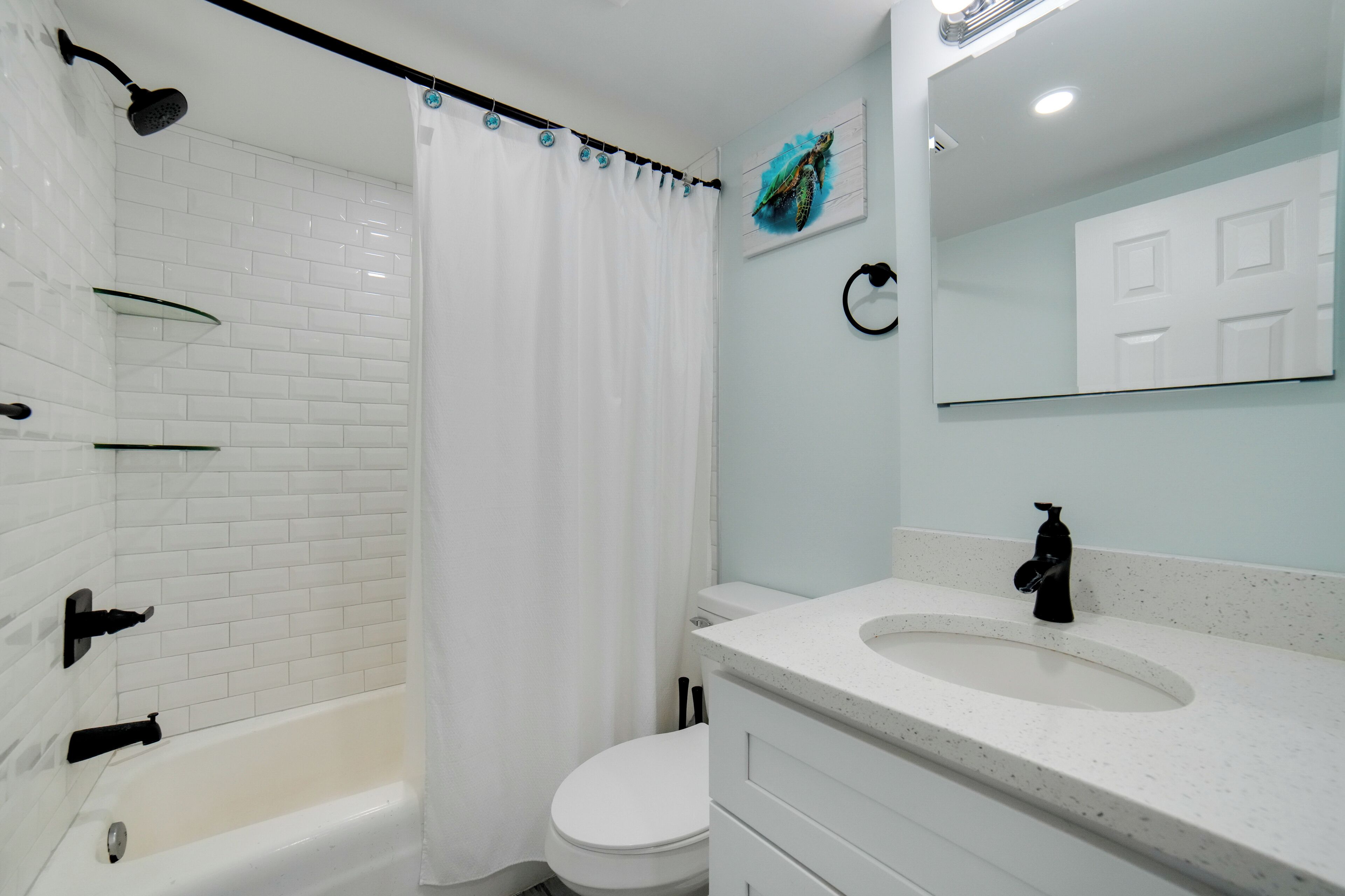 A bathroom with a white bathtub, a toilet, a sink with a mirror, and a shower curtain.