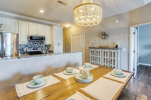 A kitchen with white cabinets, a stainless steel refrigerator, a microwave, and a wooden dining table set with bowls and placemats. - Waterfront Condo w/ Views & Pool in Little River (Little River)