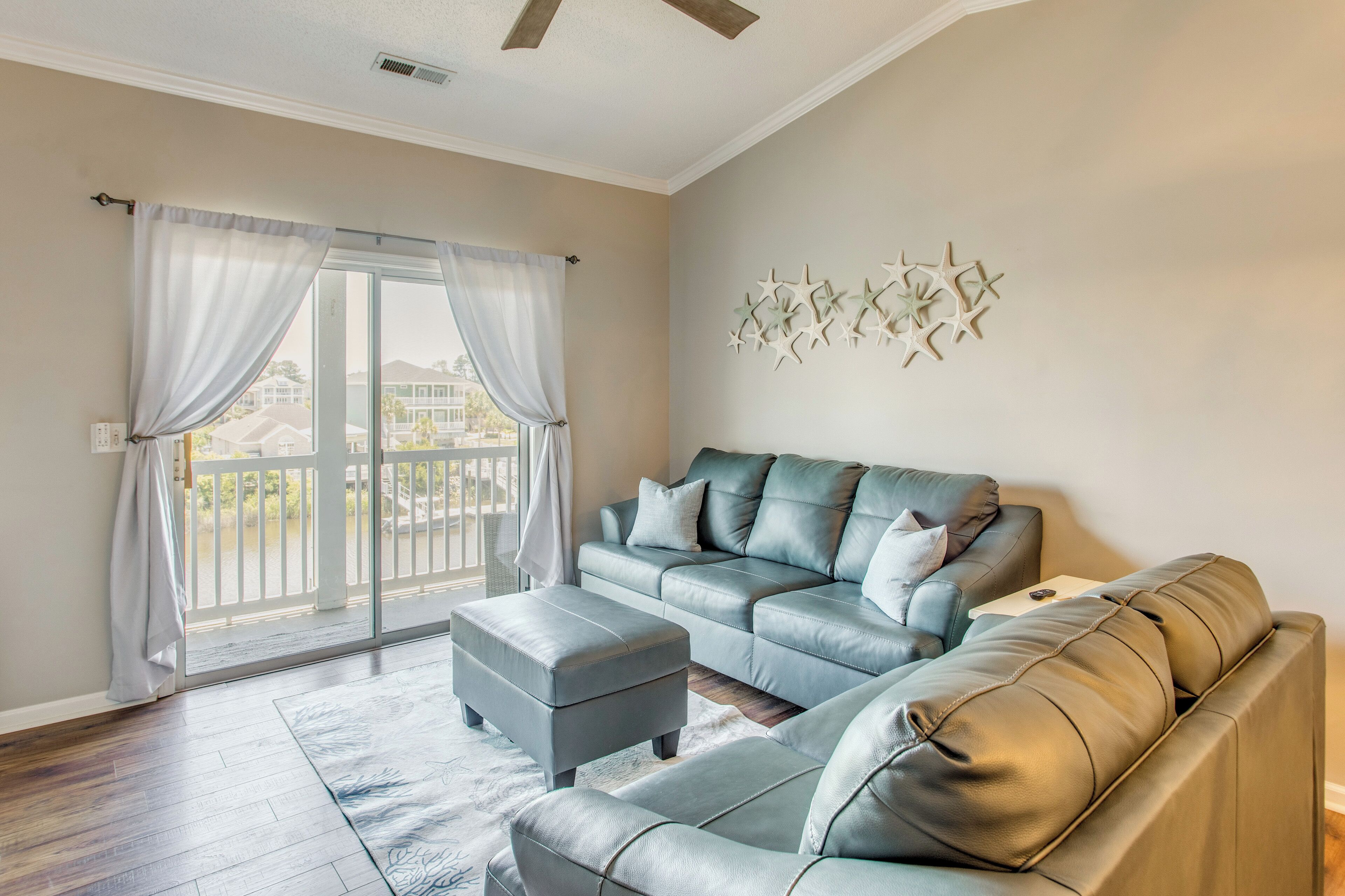 A living room with a grey sofa, ottoman, and a glass door leading to a balcony.