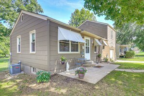 Une maison à deux étages avec un porche à l’avant, un petit jardin et un appareil de climatisation visible.