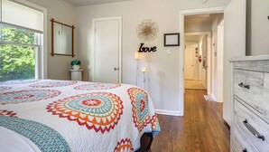 Un dormitorio con una cama grande, una mesita de noche, un aparador, un espejo, un adorno en la pared y un pasillo que conduce a otra habitación.