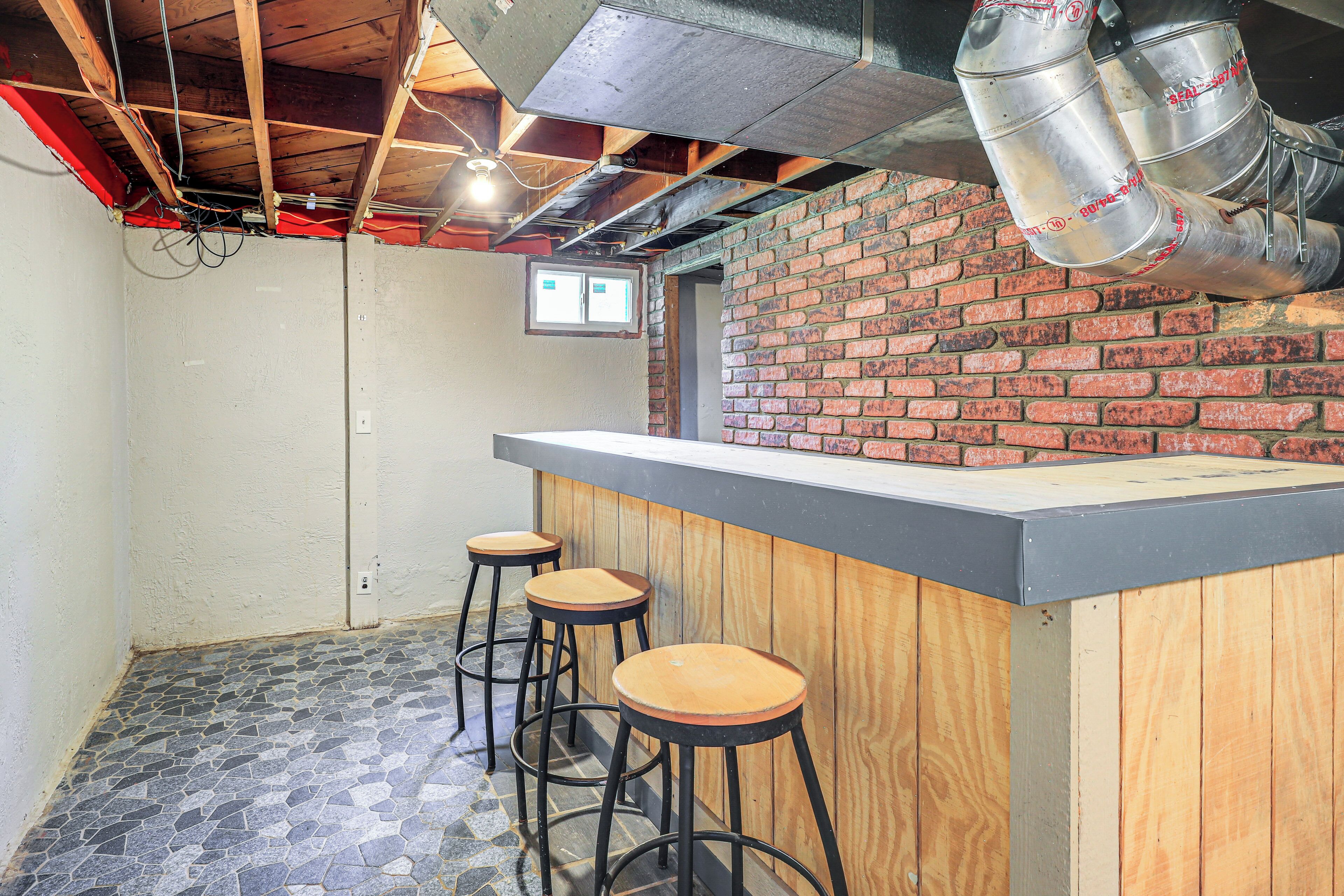 Una zona de bar con mostrador de madera, tres taburetes y pared de ladrillo.