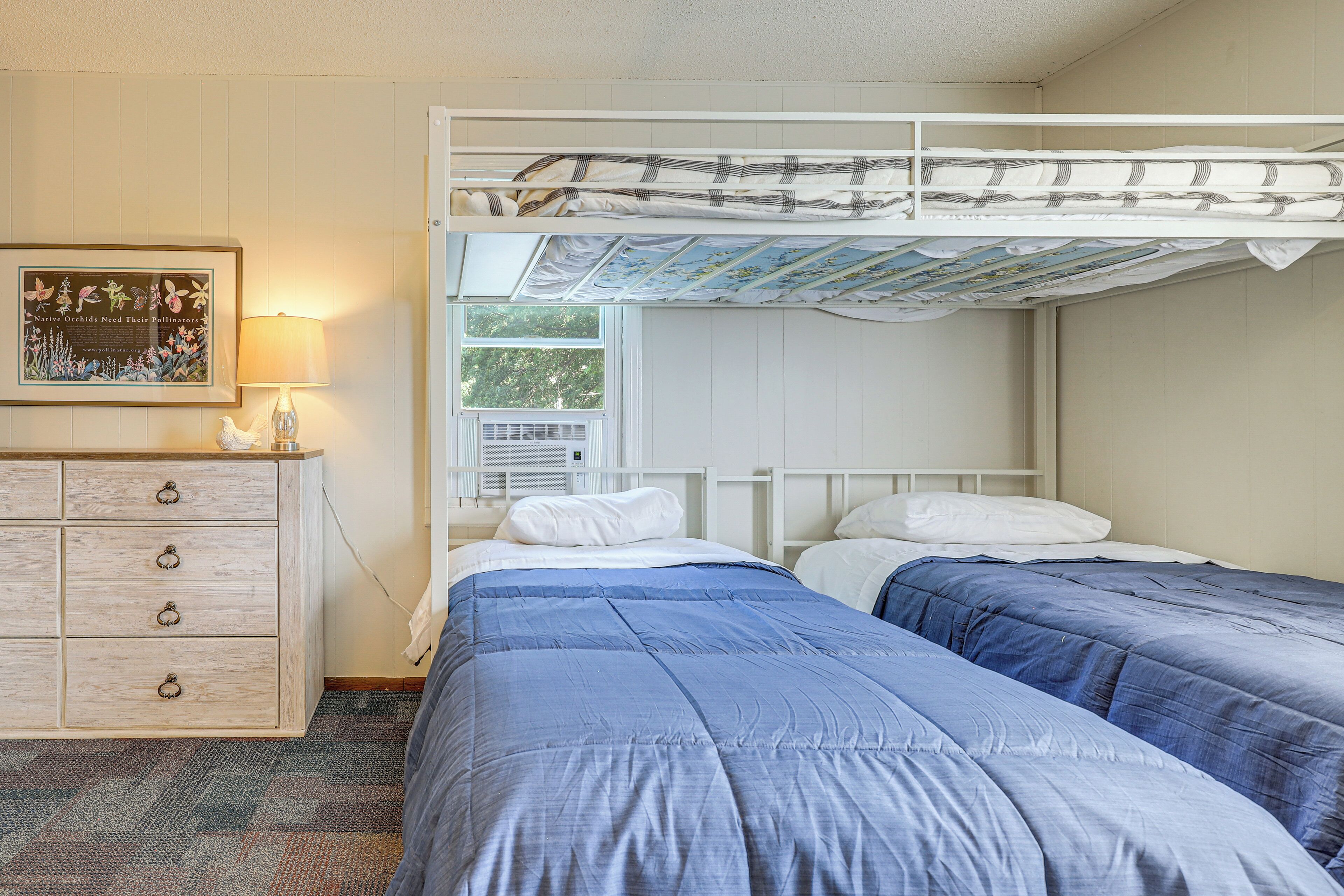 A bunk bed room with a dresser, a framed picture, and a window.
