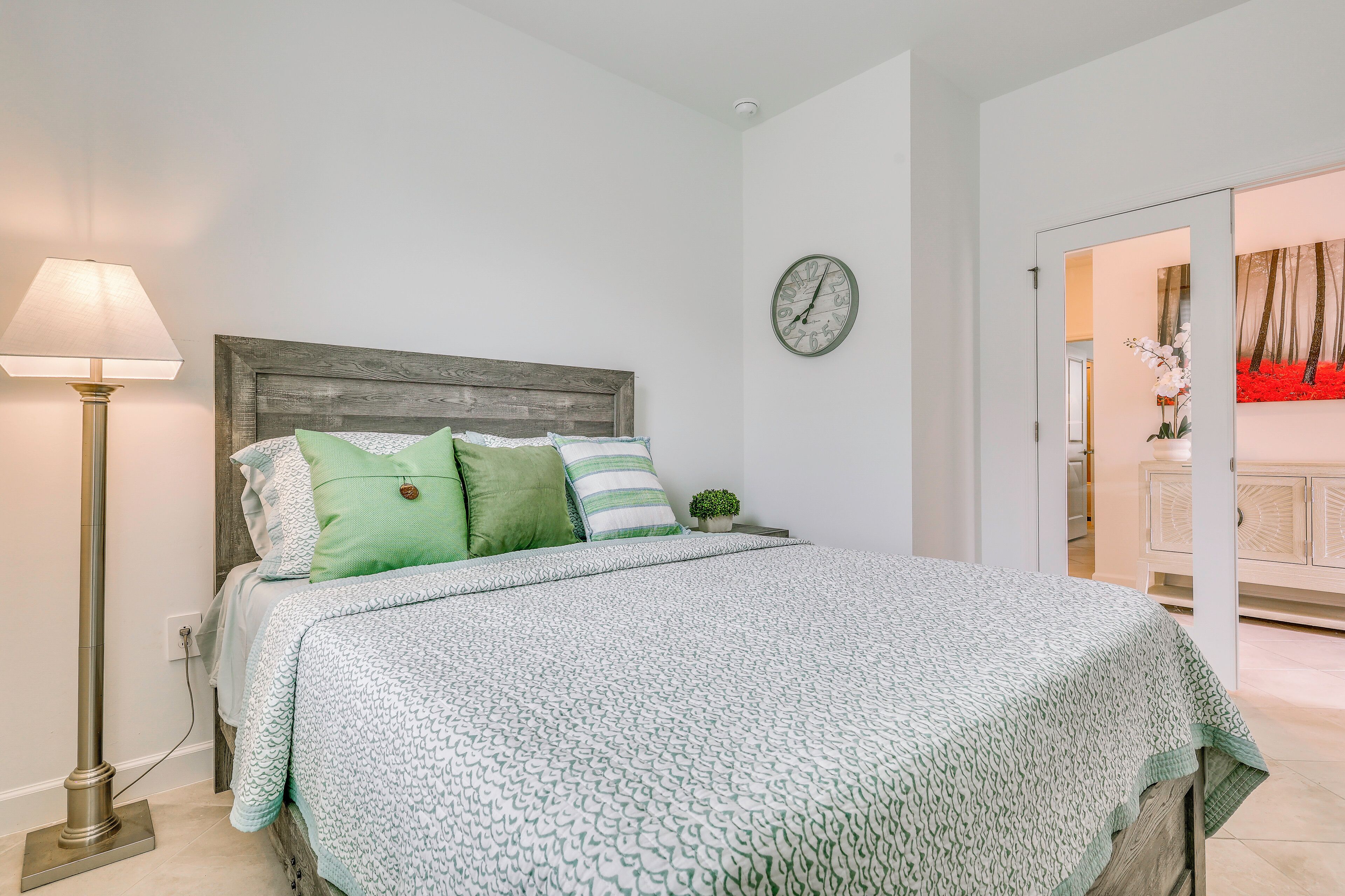 A bedroom with a bed, a bedside lamp, a clock, and a view of a hallway.