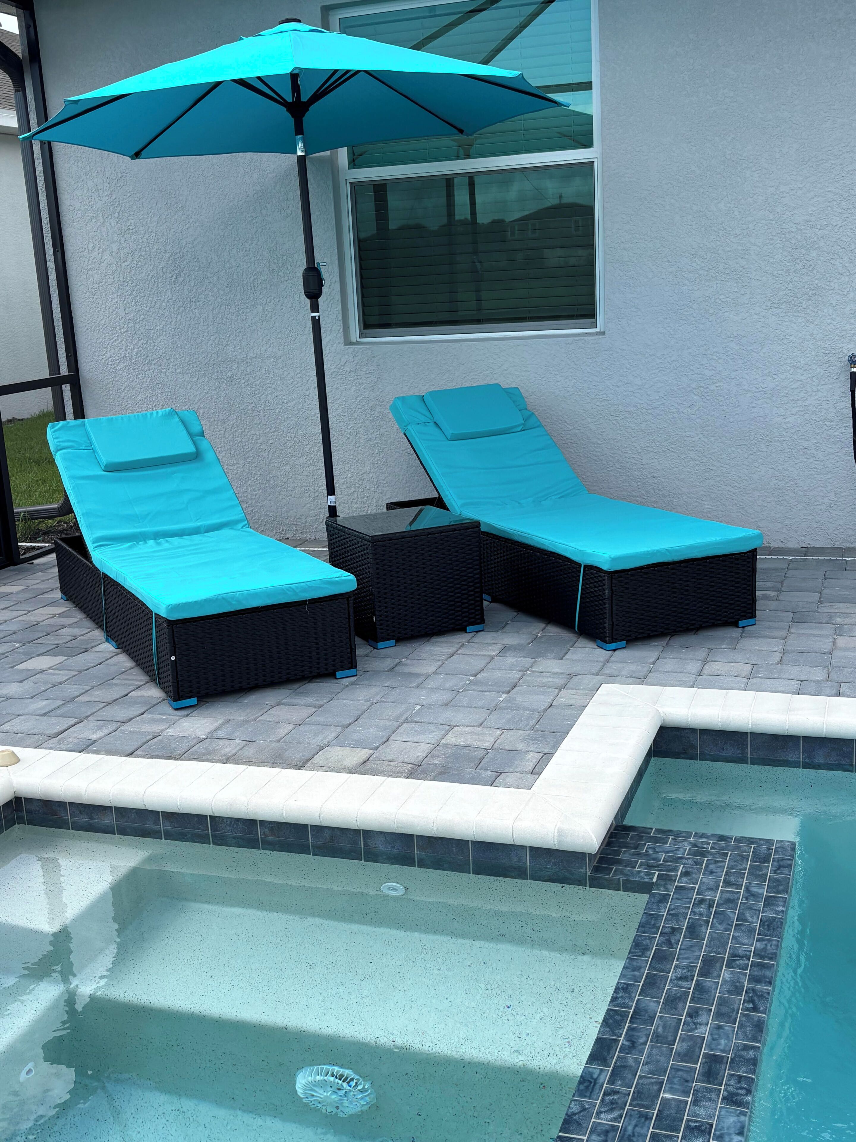 Zona de piscina amb dues gandules, un parasol blau i una piscina enrajolada.