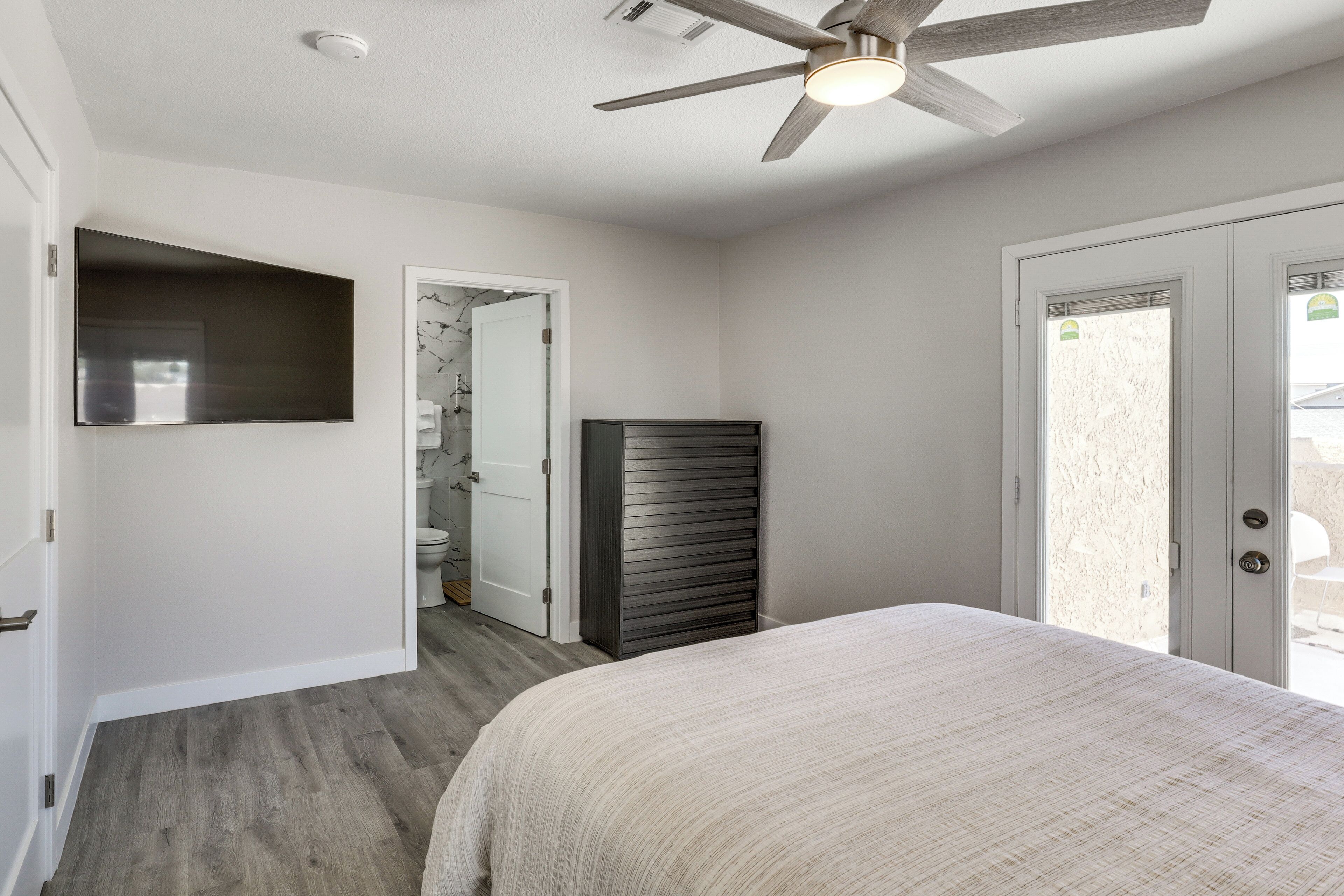 Un dormitorio con cama, ventilador de techo, armario y puerta que da a un baño.