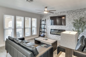 A modern living room with a sectional sofa, a coffee table, a TV mounted on a brick wall, and a ceiling fan. - 1 Mi to Unlv & Strip! Modern Vegas Condo (Las Vegas)