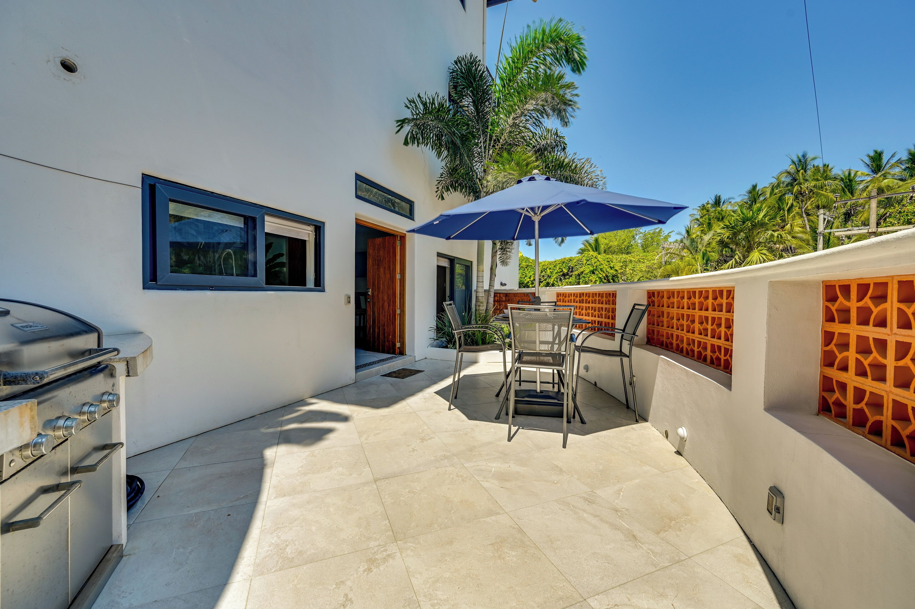 A patio with a grill, outdoor seating, and a blue umbrella.