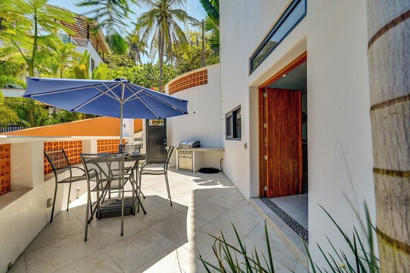 Une terrasse avec une table et des chaises, un parasol bleu et un barbecue.