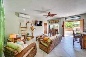 A spacious living area with wicker furniture, a ceiling fan, a TV, and a view of the outdoors.