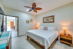A bedroom with a bed, a ceiling fan, a nightstand, a lamp, and a door leading to a balcony.