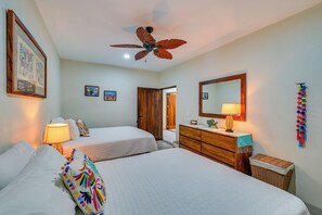 Une chambre avec deux lits, une commode en bois, un ventilateur de plafond, un miroir et des œuvres d’art murales.