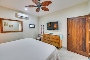 Un dormitorio con cama, cómoda de madera, televisor, ventilador de techo y armario.