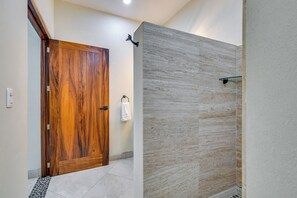 A bathroom with a wooden door, a glass shower enclosure, and a tiled floor.