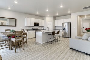 A modern kitchen with white cabinets, a stainless steel refrigerator, and a dining area with a wooden table and chairs.