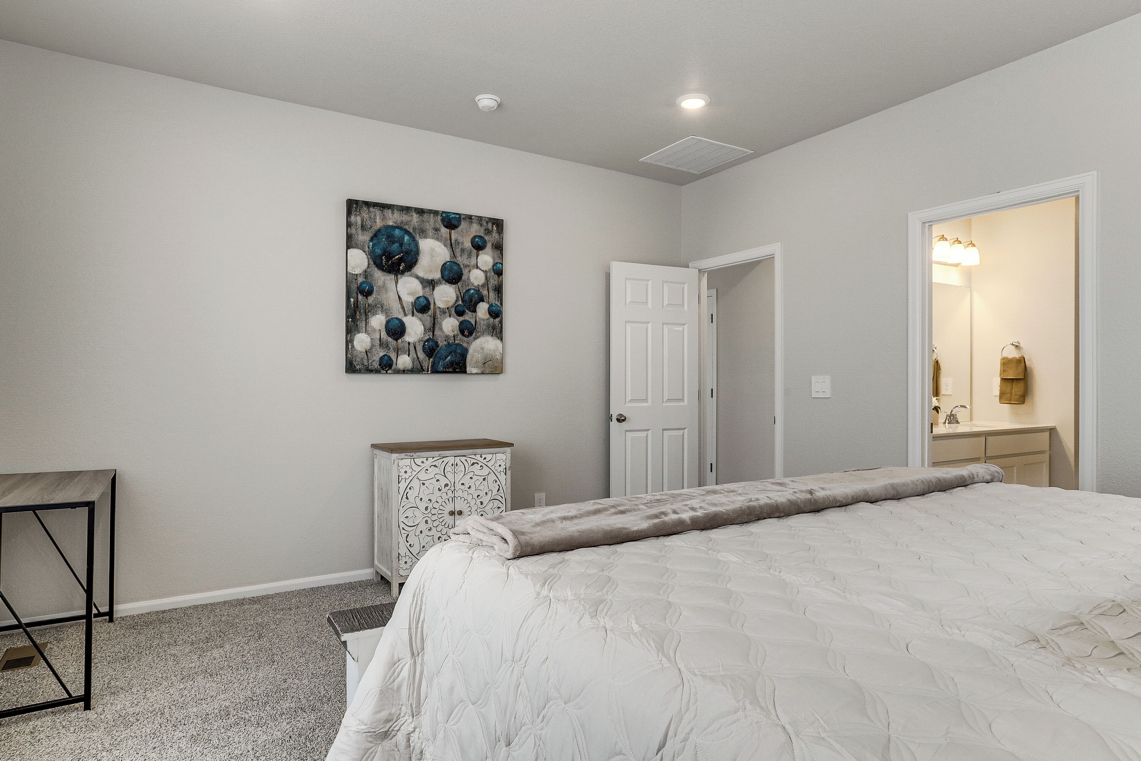 A bedroom with a bed, a dresser, a door, and a painting on the wall.