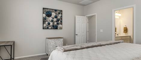 A bedroom with a bed, a dresser, a door, and a painting on the wall.