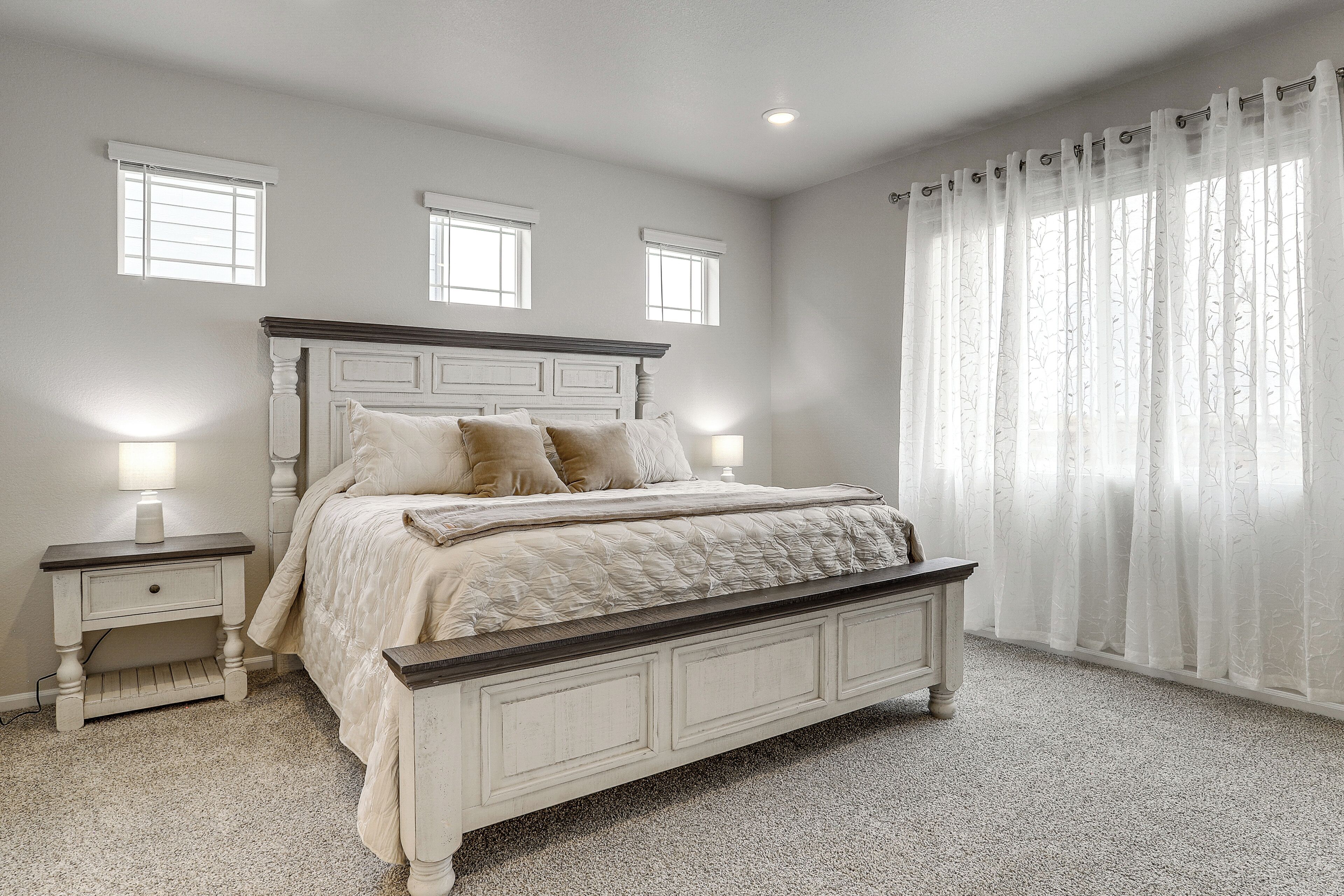 A bedroom with a bed, nightstands, a window with curtains, and a carpeted floor.