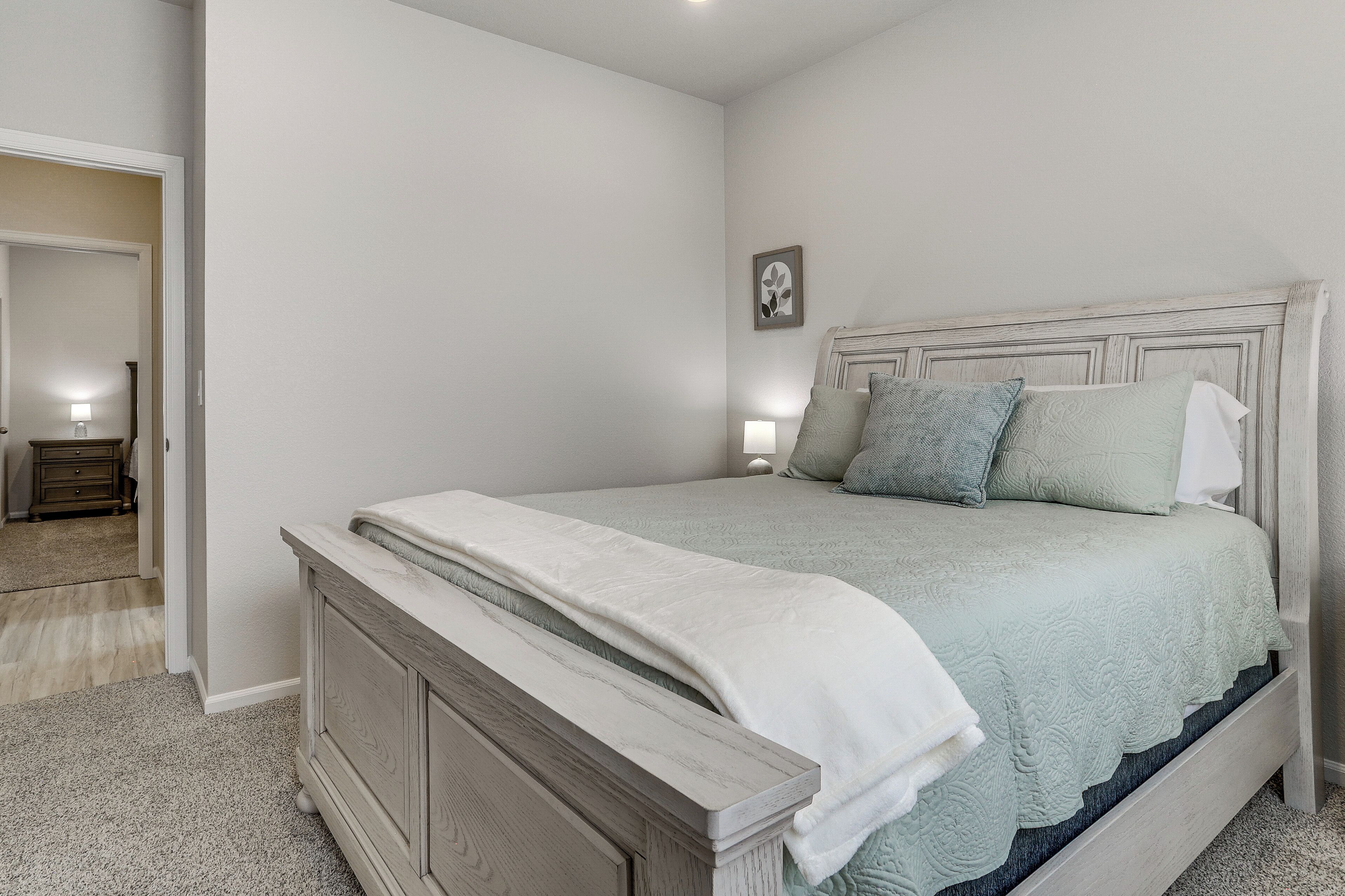 A bedroom with a bed, bedside lamps, and a door leading to another room.