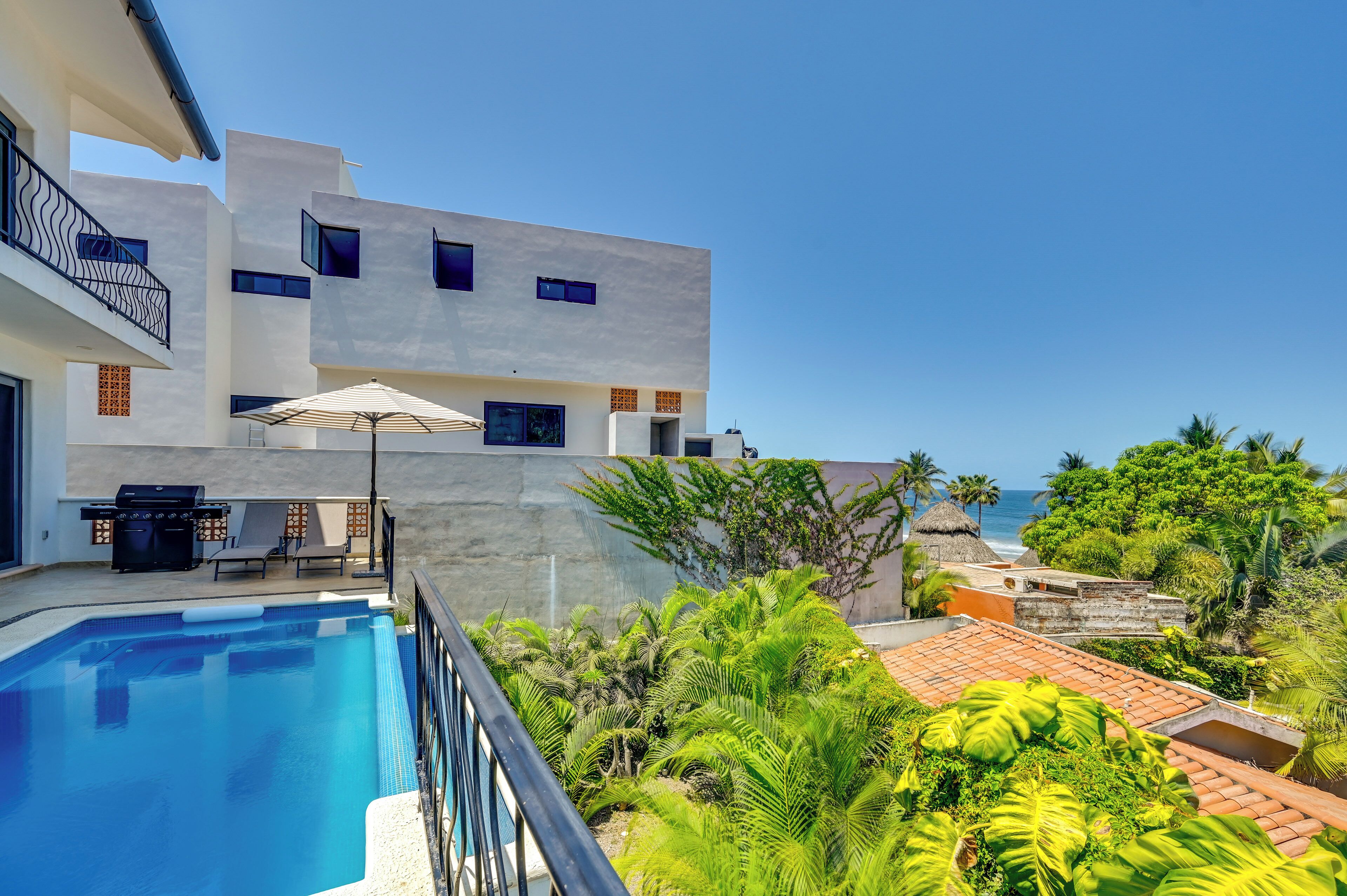 Un edificio moderno con piscina, mobiliario exterior y vista al océano.