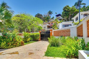 A pathway leading to a gated entrance with lush greenery and a multi-story building with balconies. - Infinity Pool & Concierge: Private San Pancho Home (San Francisco)