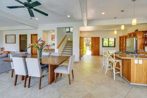 A spacious living area with a dining table, chairs, a sofa, a ceiling fan, and a kitchen with wooden cabinets and a refrigerator.
