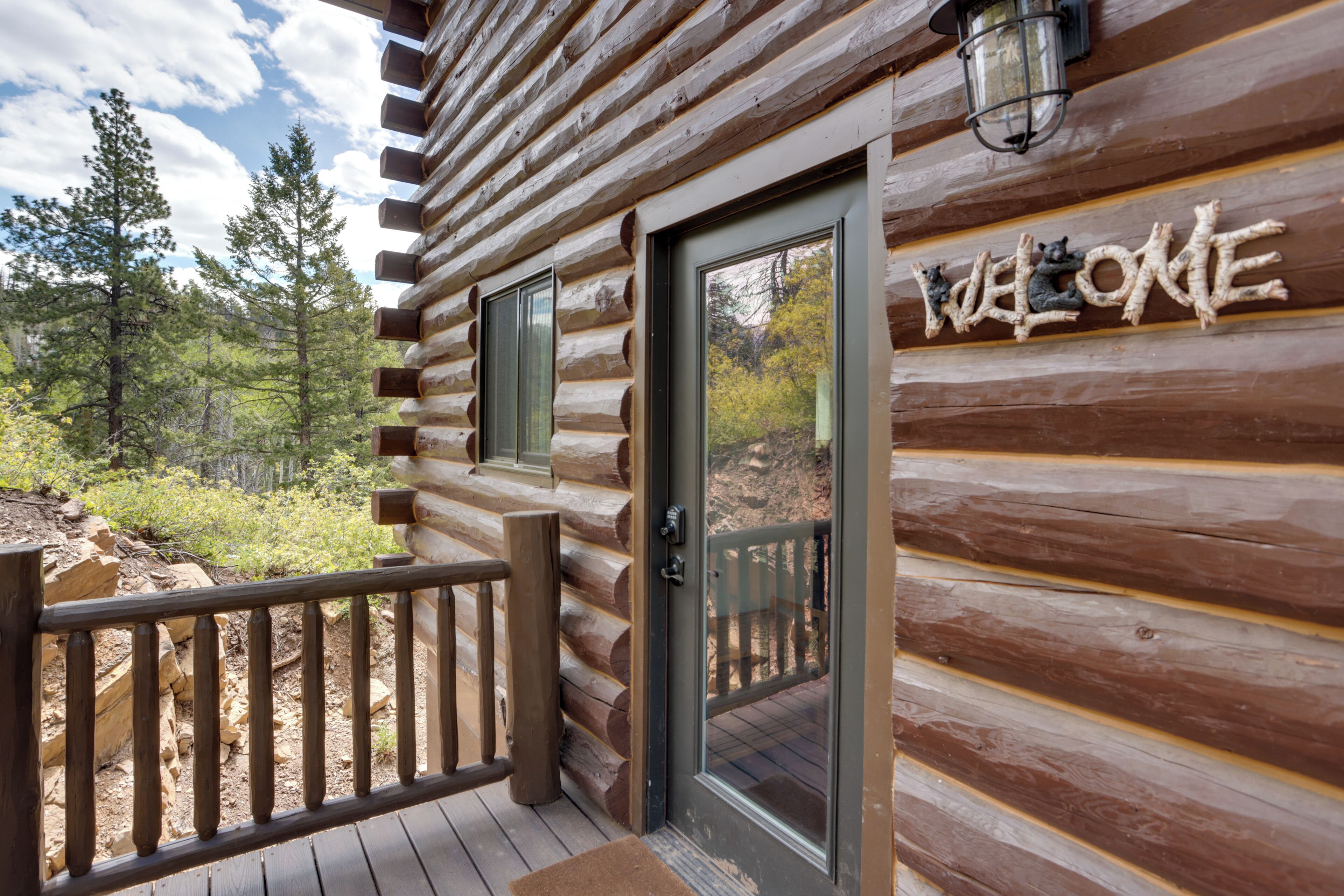 A log cabin with a wooden deck and a 'WELCOME' sign.
