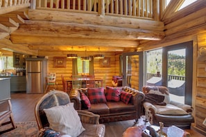 A log cabin interior with a wooden staircase, a dining area, a sofa with plaid cushions, and a view through large windows. - Durango Mountain Escape w/ Stunning Views (Durango)