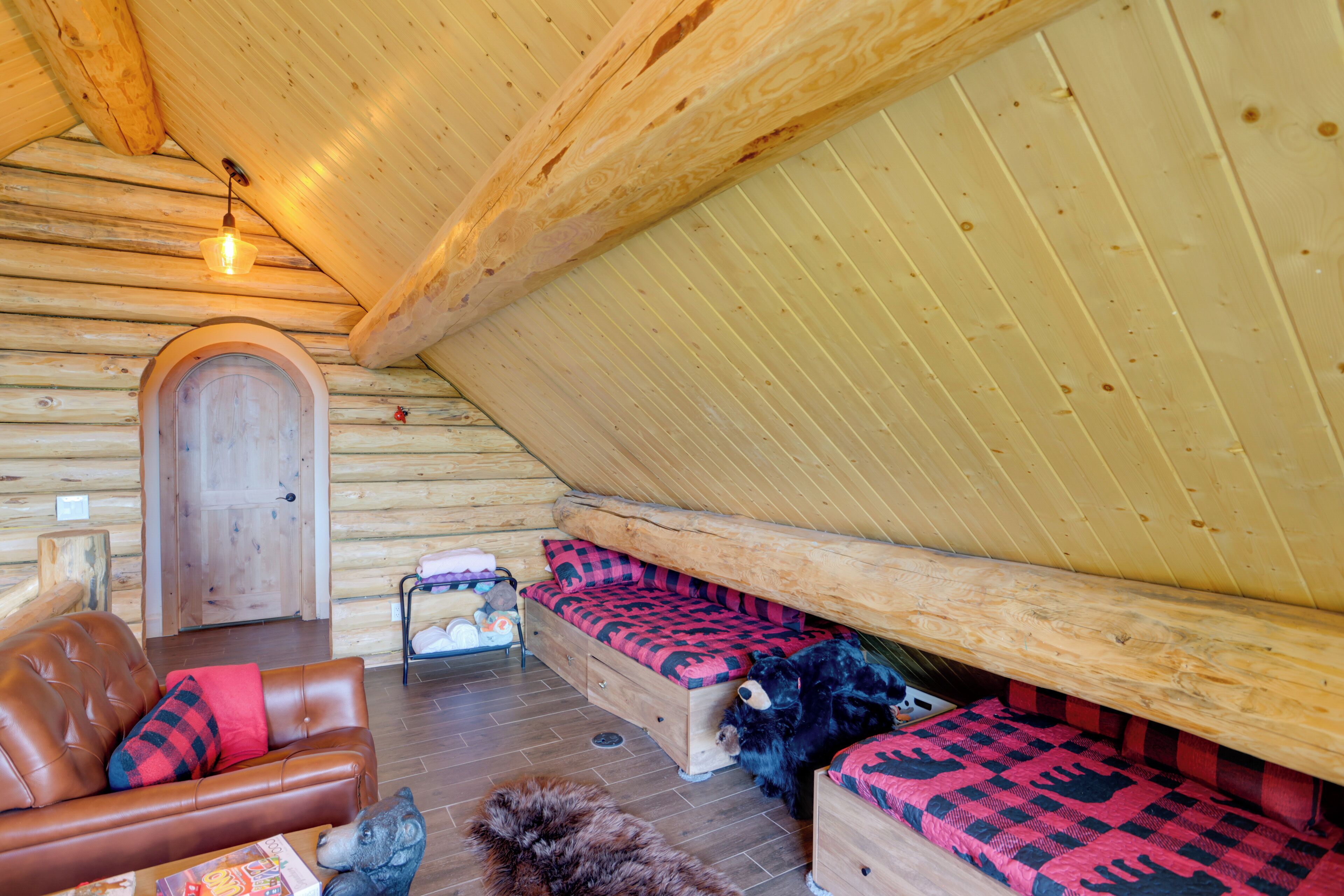 A log cabin interior with a loft bed, a sofa, a wooden door, and a light fixture.