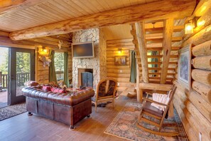 A log cabin interior with a stone fireplace, leather sofa, rocking chair, and wooden walls. - Durango Mountain Escape w/ Stunning Views (Durango)