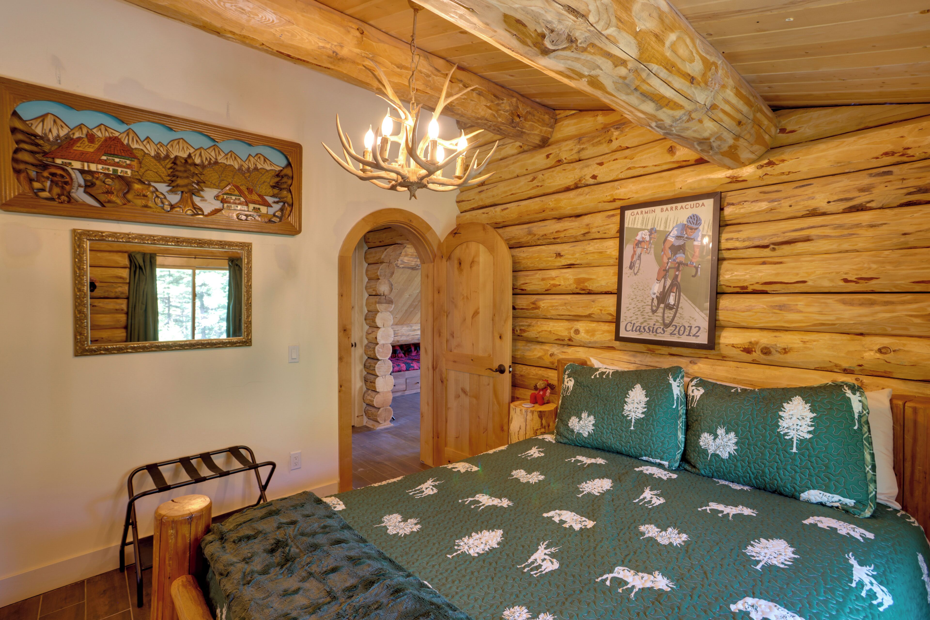 A log cabin room with a bed, a chandelier, a framed picture, and a mirror.