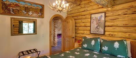 A log cabin room with a bed, a chandelier, a framed picture, and a mirror.