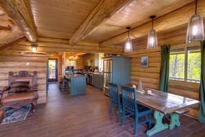 Ein rustikales Blockhaus im Inneren mit Essbereich, Küche und Blick ins Freie.