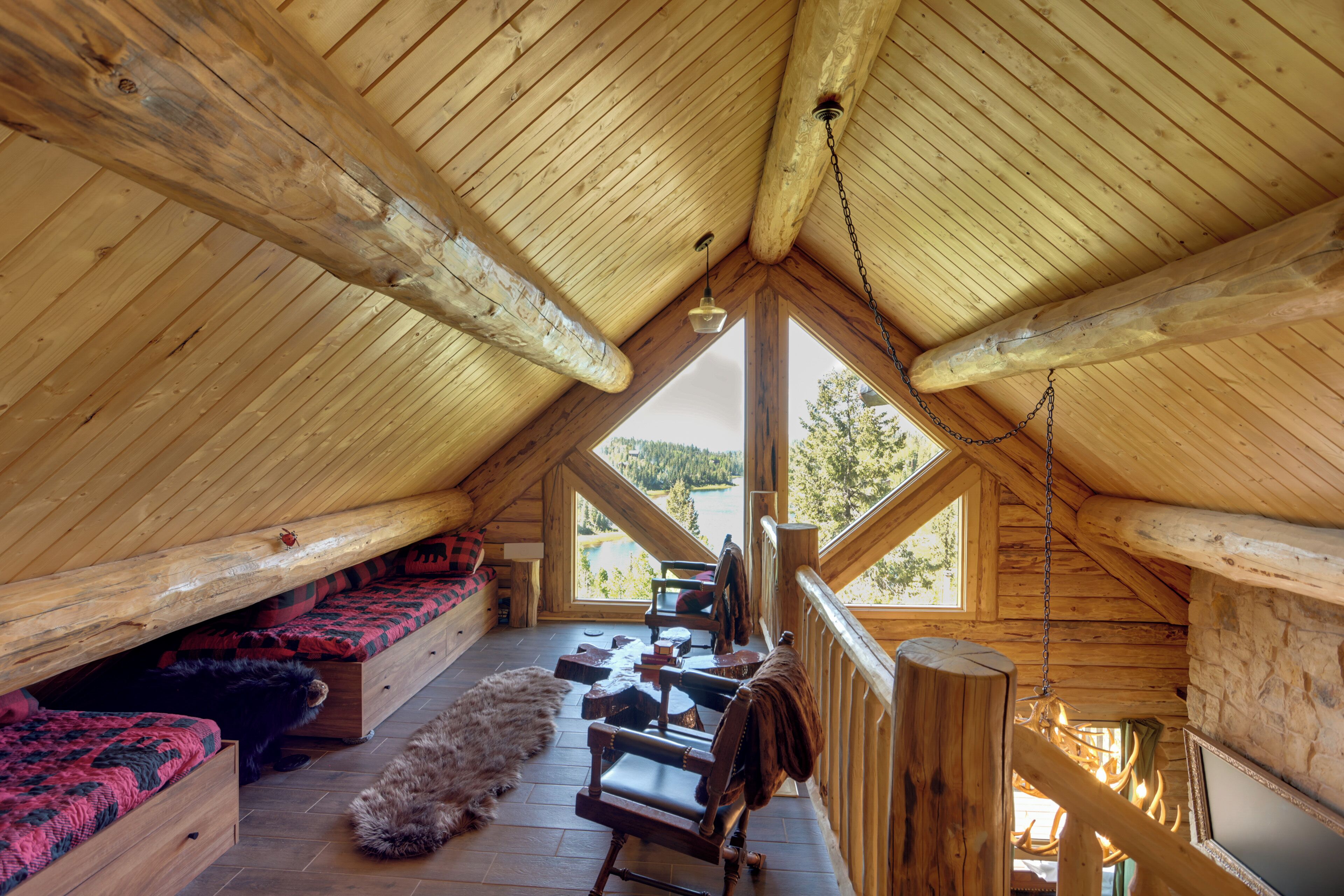 A wooden attic room with a sloped ceiling, a wooden bench, a chair, a fur rug, and a view of the outdoors.