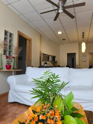 Een woonkamer met een witte bank, een plafondventilator en een bloempot met oranje bloemen.