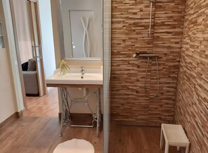 Een badkamer met een wastafel, spiegel, douche en houten wand.