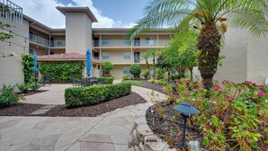 A courtyard with a palm tree, outdoor seating, and a building with balconies. - Golf On-site! Extended Stay 4 Mi to Dtwn Naples (Naples)