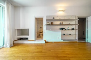 A room with a wooden floor, a white wall, a built-in shelf unit, and a door leading to a bathroom. - K K Villa in Athens Riviera With Private Pool (Vari-Voula-Vouliagmeni)