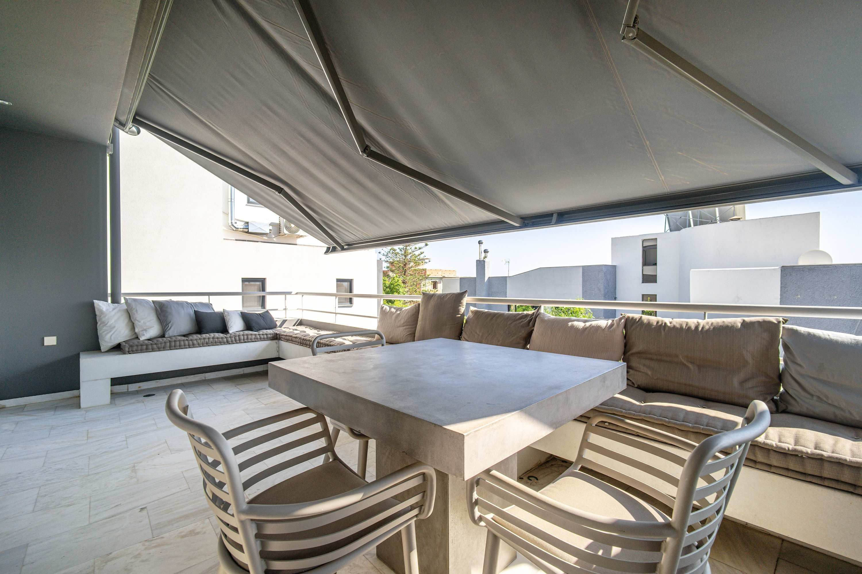 Un patio al aire libre con una mesa, sillas, un sofá y un toldo grande.