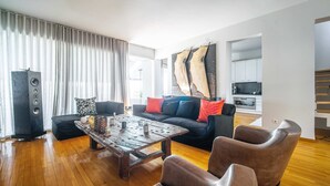 Een woonkamer met een zwarte bank, een houten salontafel, leren fauteuils en een grote speaker.