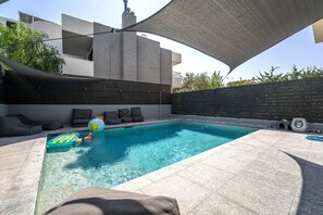 A swimming pool with a sunshade, lounge chairs, and a small inflatable pool.