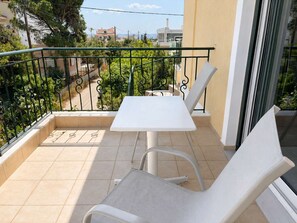 A balcony with a table and two chairs, a tiled floor, and a view of greenery and buildings. - Artemida Olive Gem - Sunny Balcony Views Parking (Spata-Artemida)