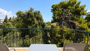A balcony with a white table and two chairs, surrounded by a metal railing and lush greenery.
