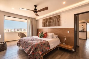 Ein modernes Hotelzimmer mit einem großen Bett, einem Deckenventilator, einem Blick durch einen Balkon und einem Holzkopfende.